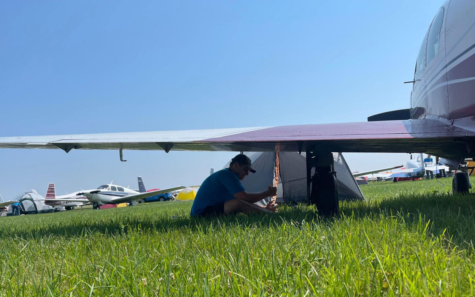 Upon arrival at the Oshkosh, Wisconsin EAA AirVenture air show, Mooney Caravan members camp underneath the wings of their airplanes.