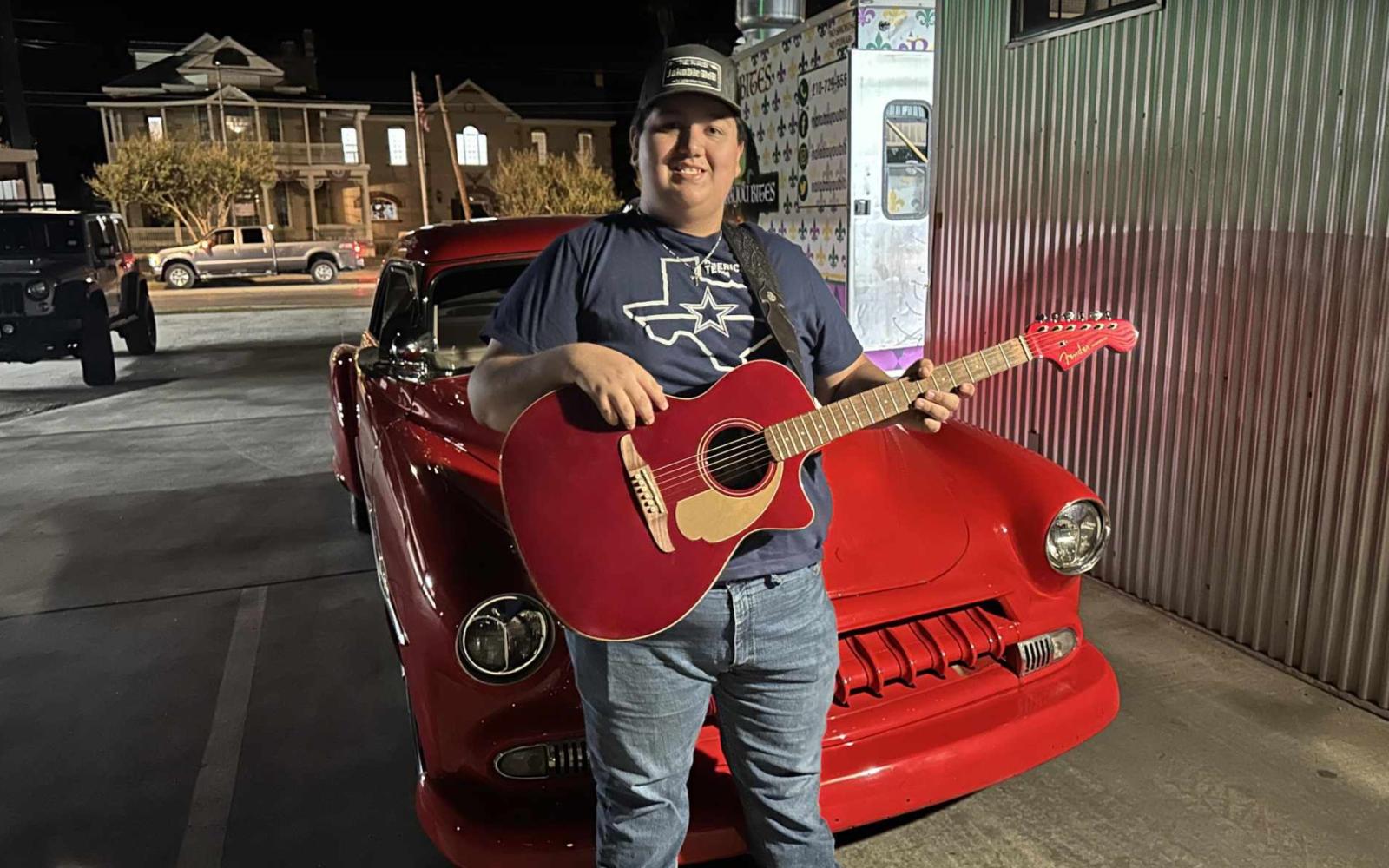 Jakobie Bell posing with his guitar against car