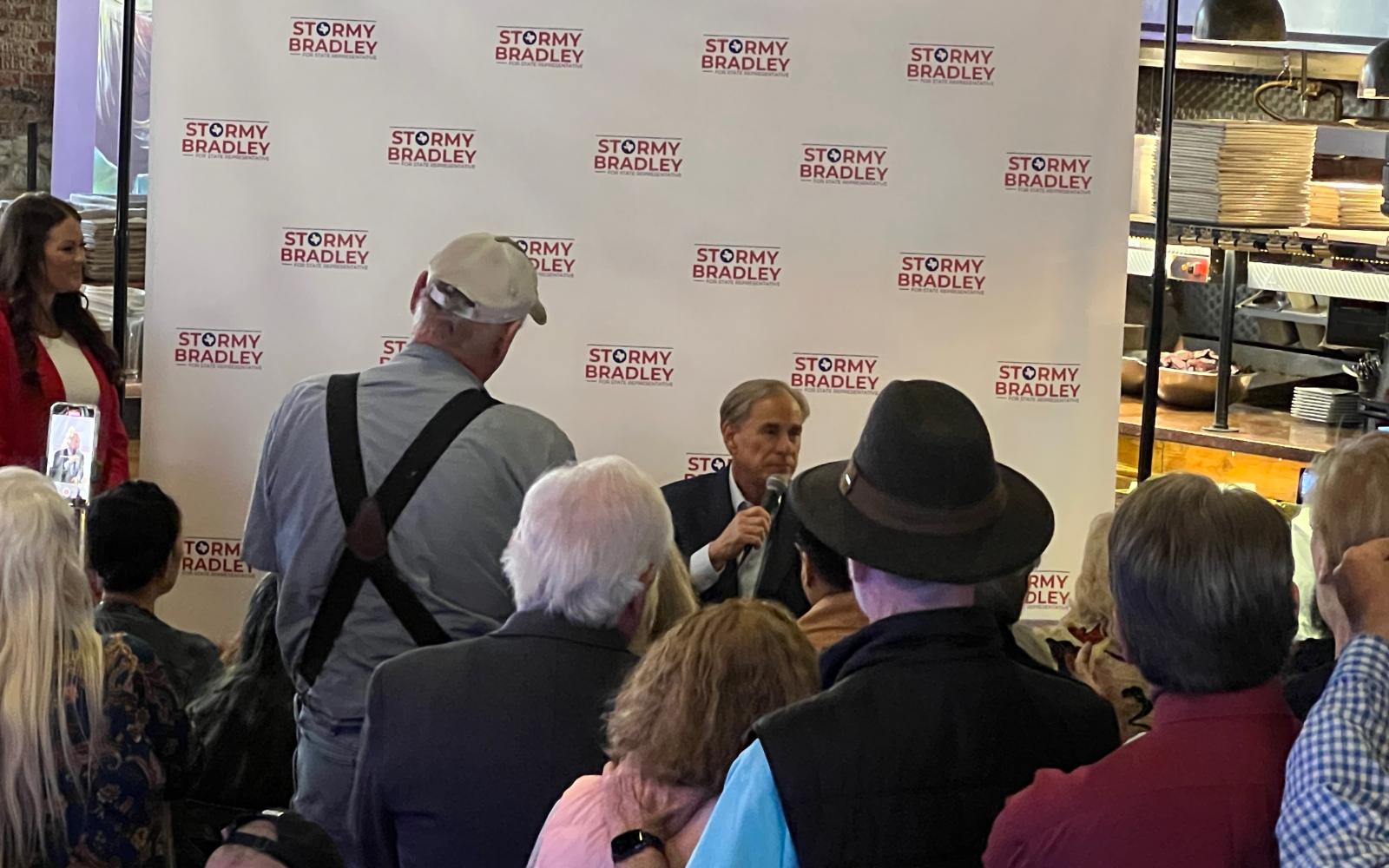Gov. Greg Abbott speaks to a crowd at the Angry Cactus where Abbott was campaigning for Rep. Drew Darby's opponent, Stormy Bradley, who is looking on from the left on Feb. 23, 2024.